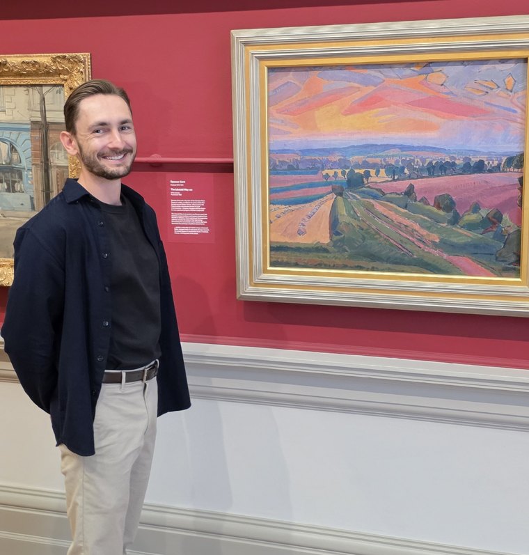 Bastien smiling beside a landscape painting in a gallery